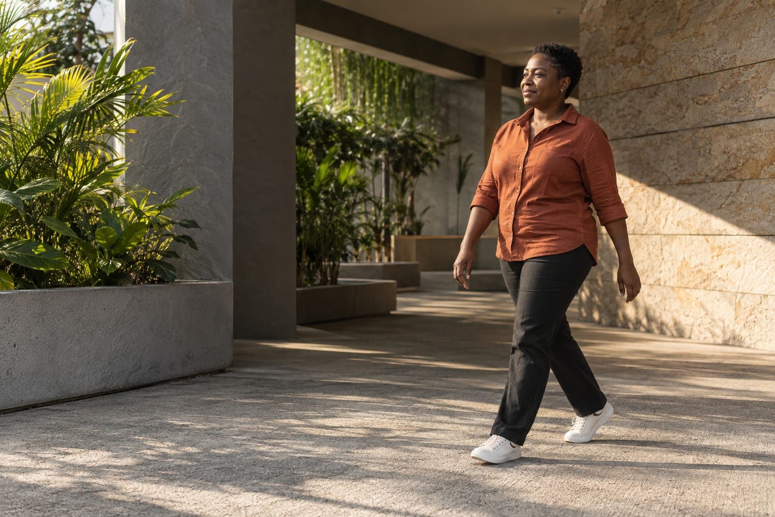 A woman walks along a shaded concrete walkway in the afternoon sun.