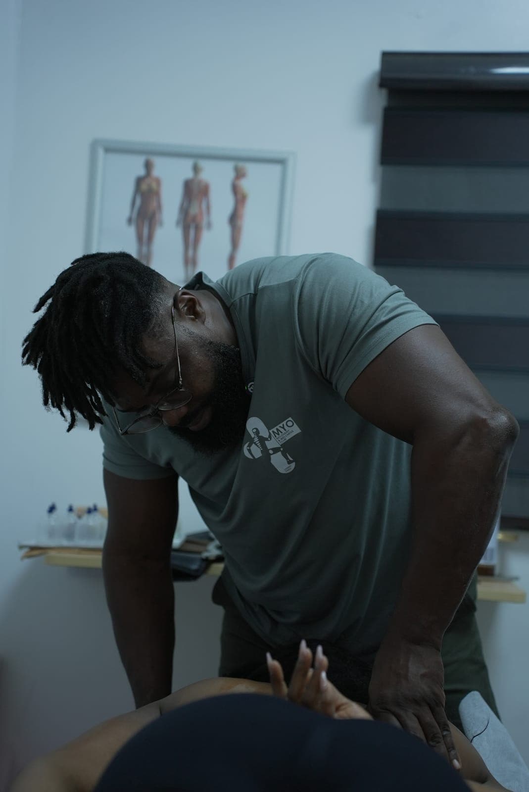 A MYO therapist in the MYO shirt concentrating on a treatment, the anatomy chart behind him